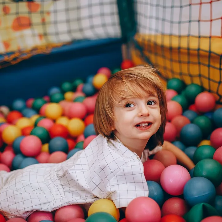 A smiling child playing in a colourful indoor ball pit