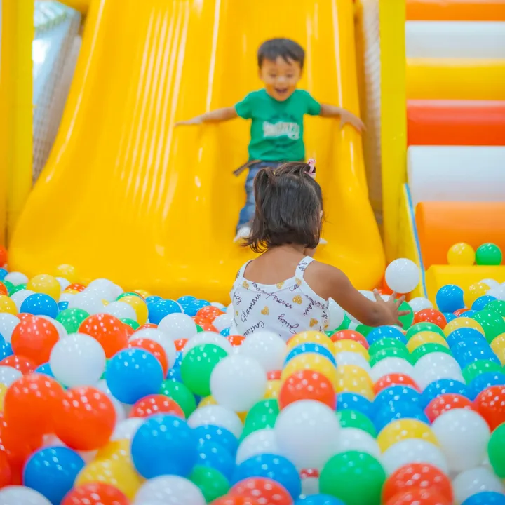 Children playing on yellow indoor slides beside a colourful ball pit